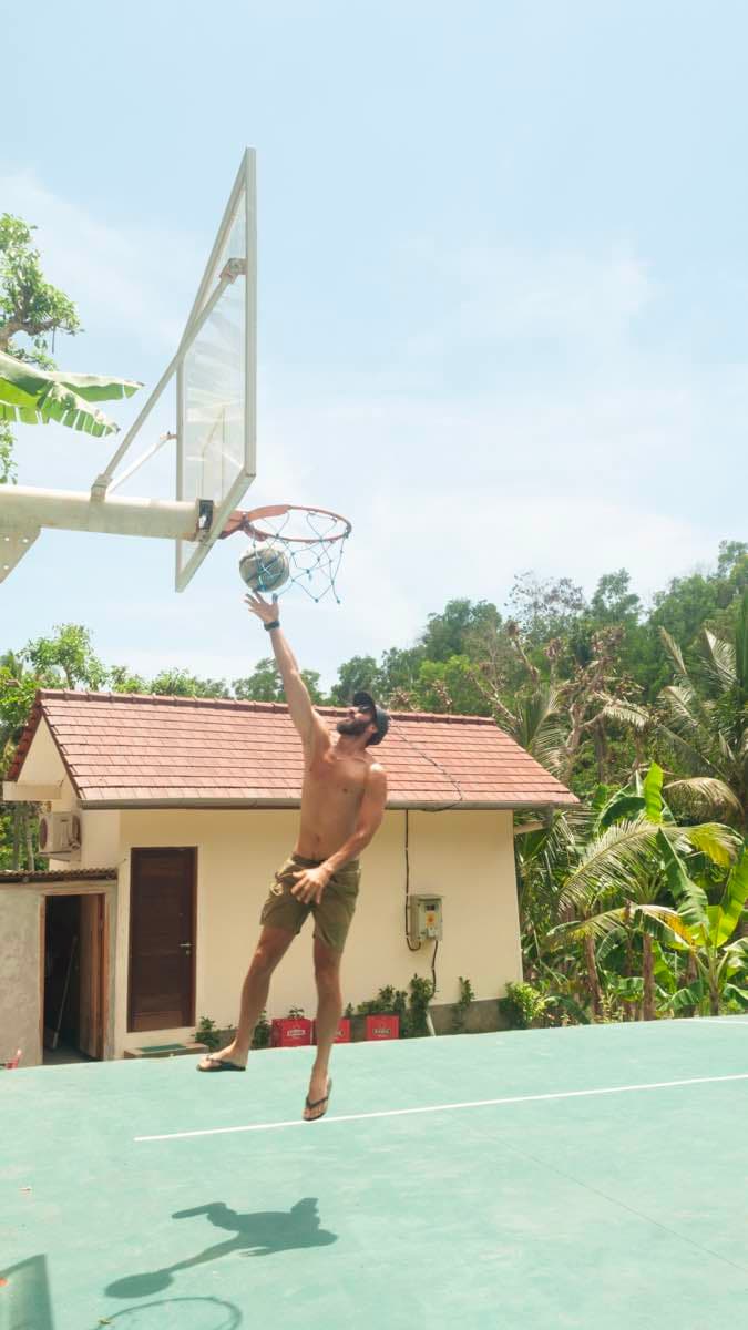 Energetic group of remote workers and digital nomads playing an evening basketball game at The Penida Project community sports facilities in Nusa Penida