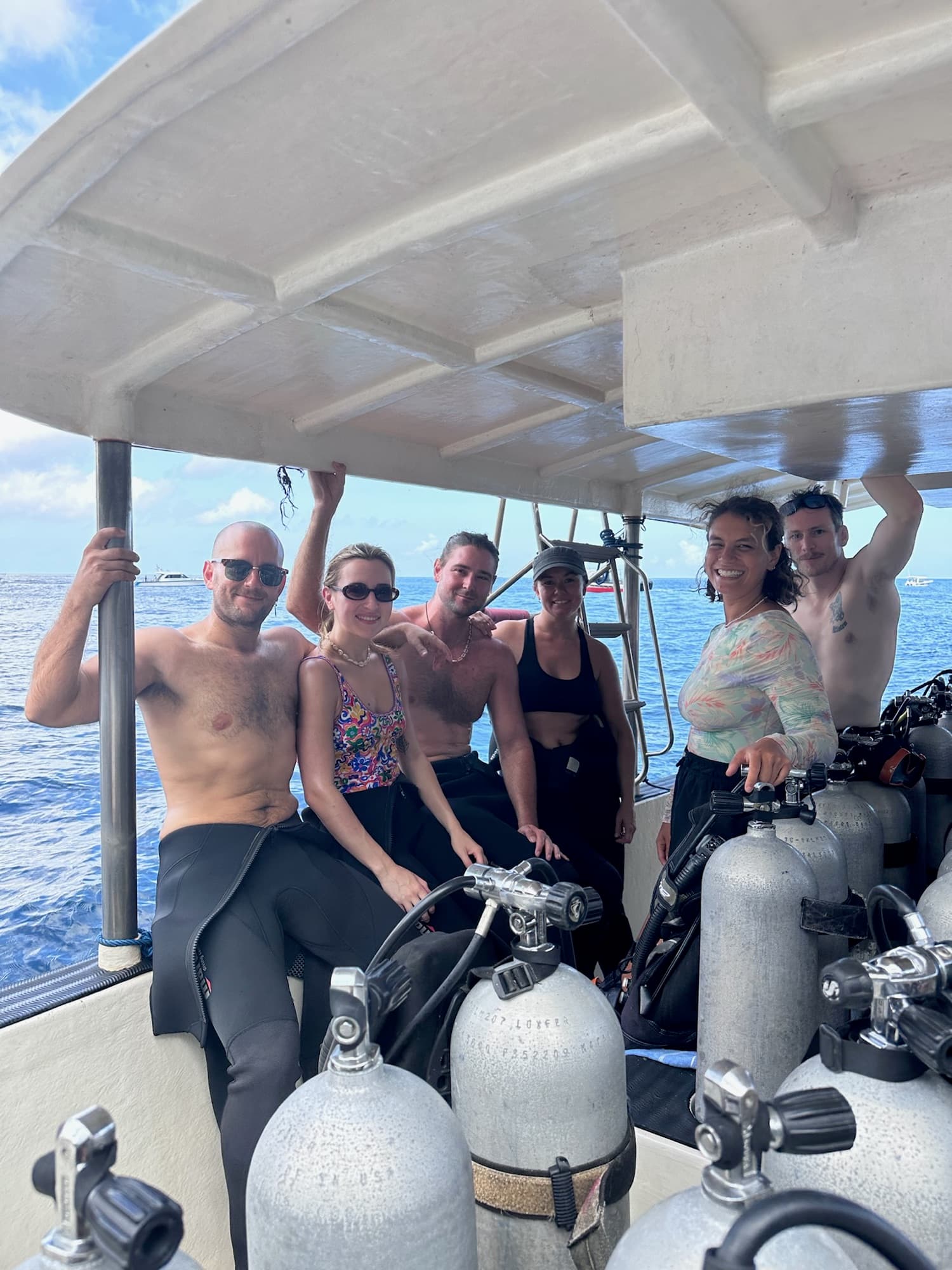 Divers from Project Laut smiling together aboard a dive boat in Nusa Penida with scuba tanks ready for the water